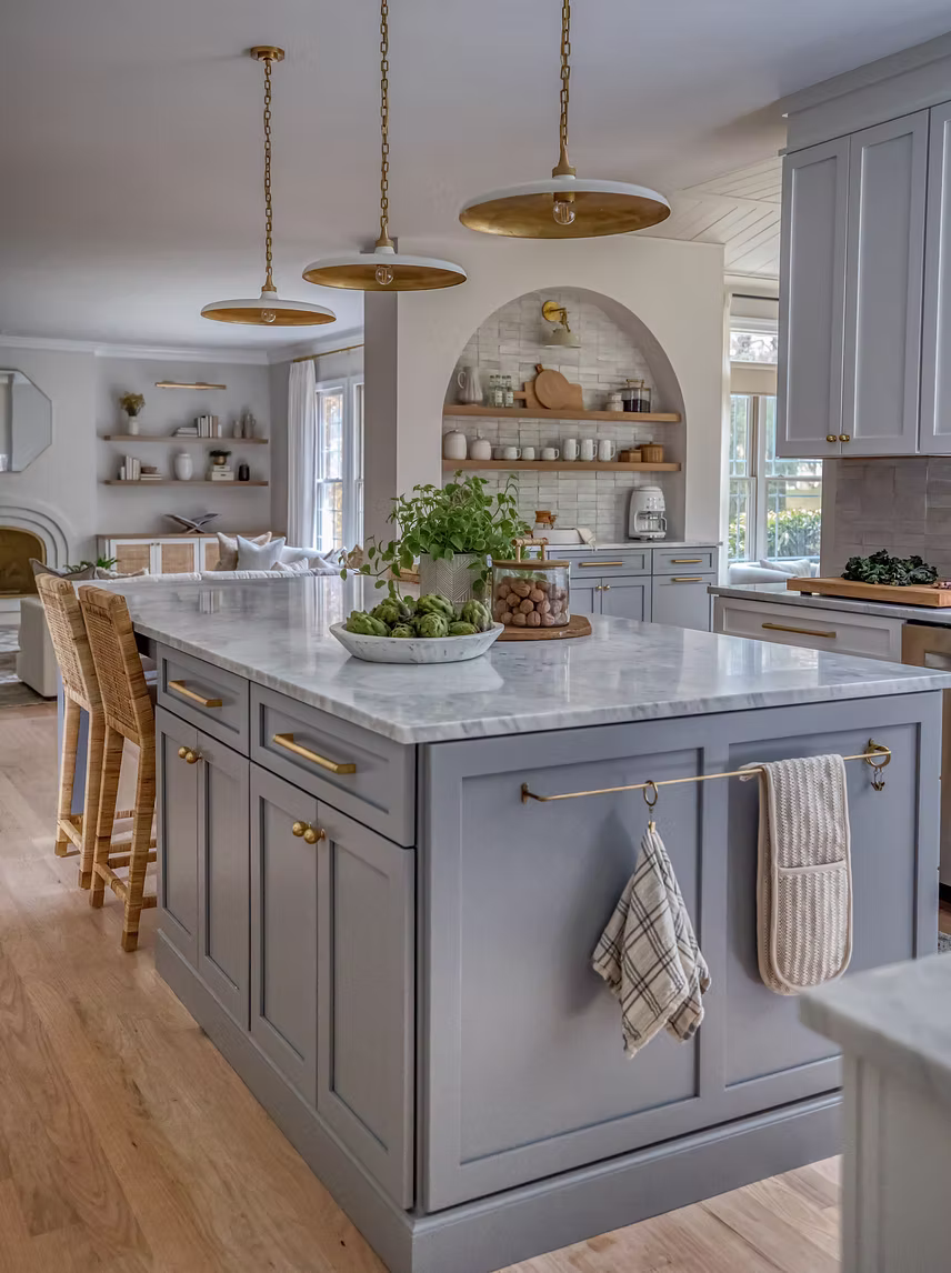 Angle view of soft blue kitchen island with brass towel rack and marble countertop looking toward an arched scullery in Rockville MD by Sho and Co Cabinetry