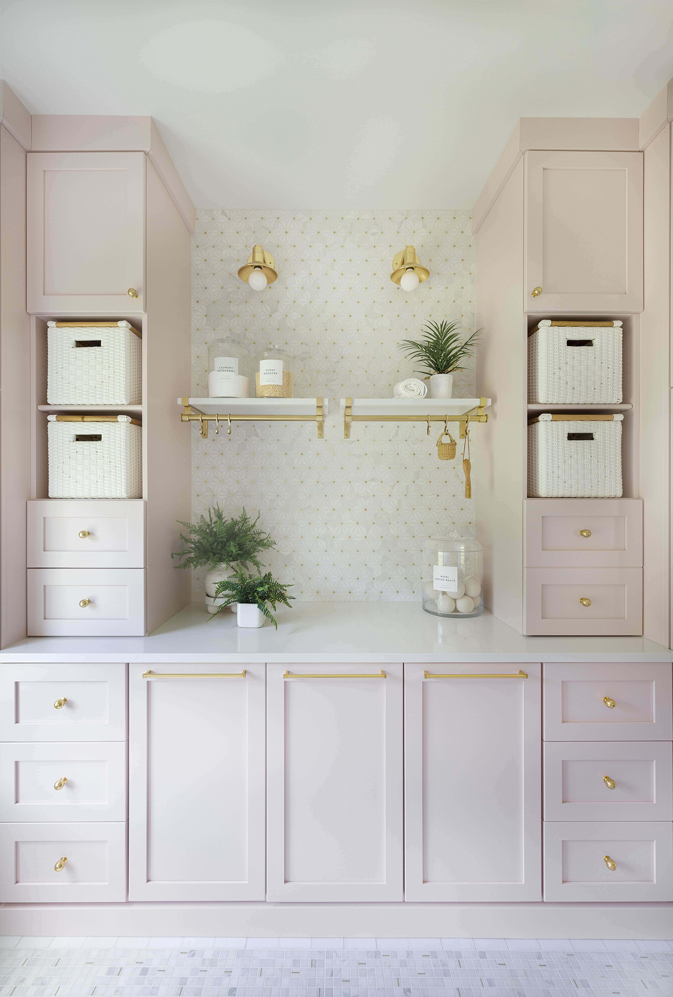 Symmetrical elevation of custom soft blush laundry room cabinetry with twin storage towers, brass sconces, and marble mosaic backsplash by Sho and Co Cabinetry