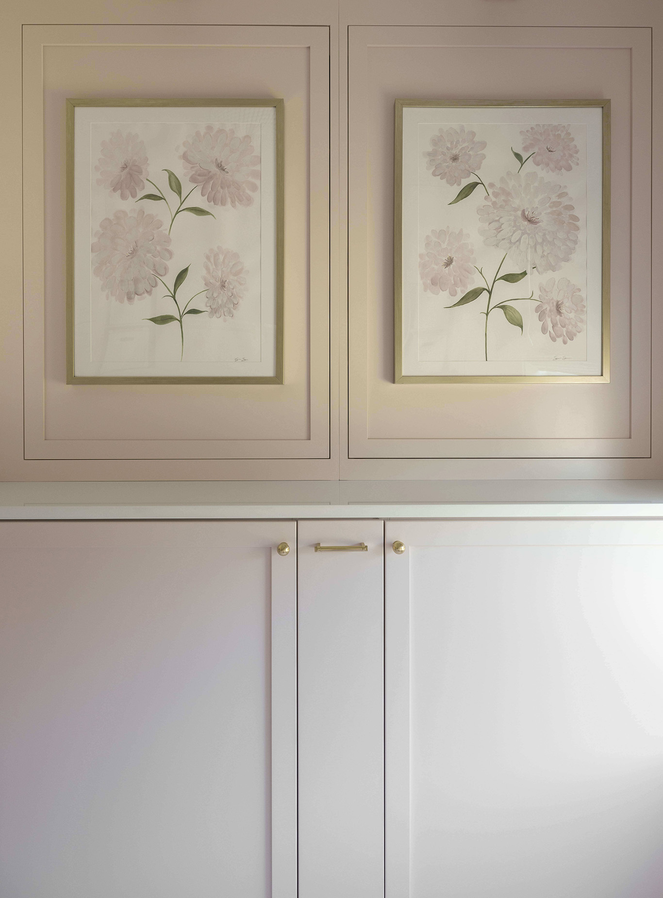Detail view of custom blush laundry room upper cabinetry with framed botanical artwork panels integrated into cabinet doors by Sho and Co Cabinetry