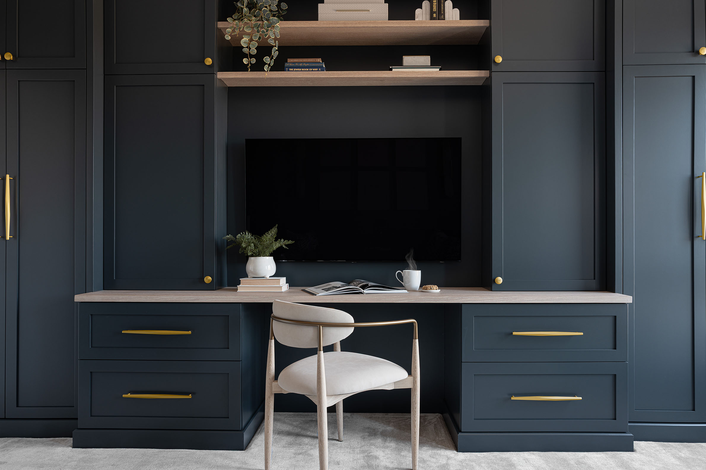 Dark navy built-in home office desk and TV entertainment unit with light oak desktop and brass hardware at The Grandview in North Bethesda MD by Sho and Co Cabinetry